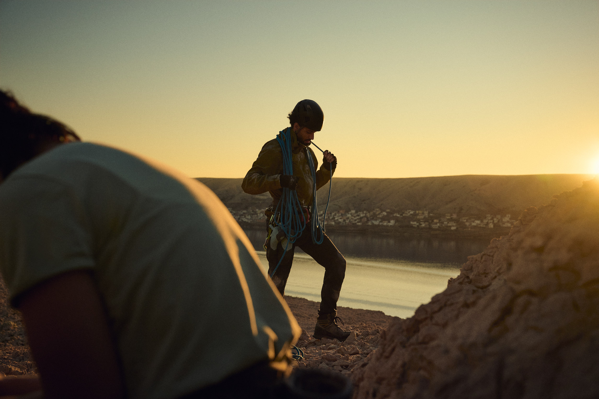 Climber carrying rope across rocky ground in low sun.