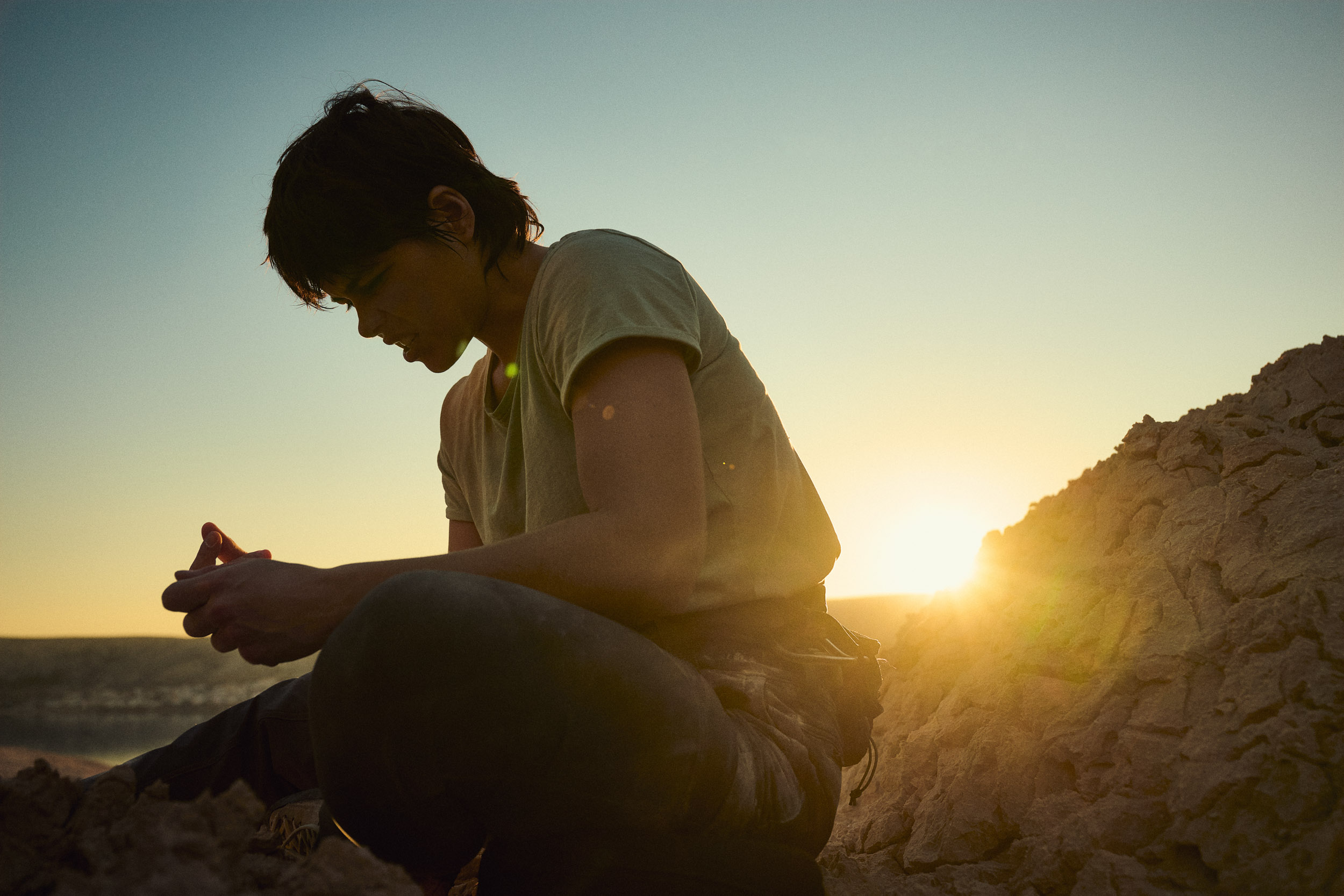 Climber resting against a mountain backdrop with taped fingers.