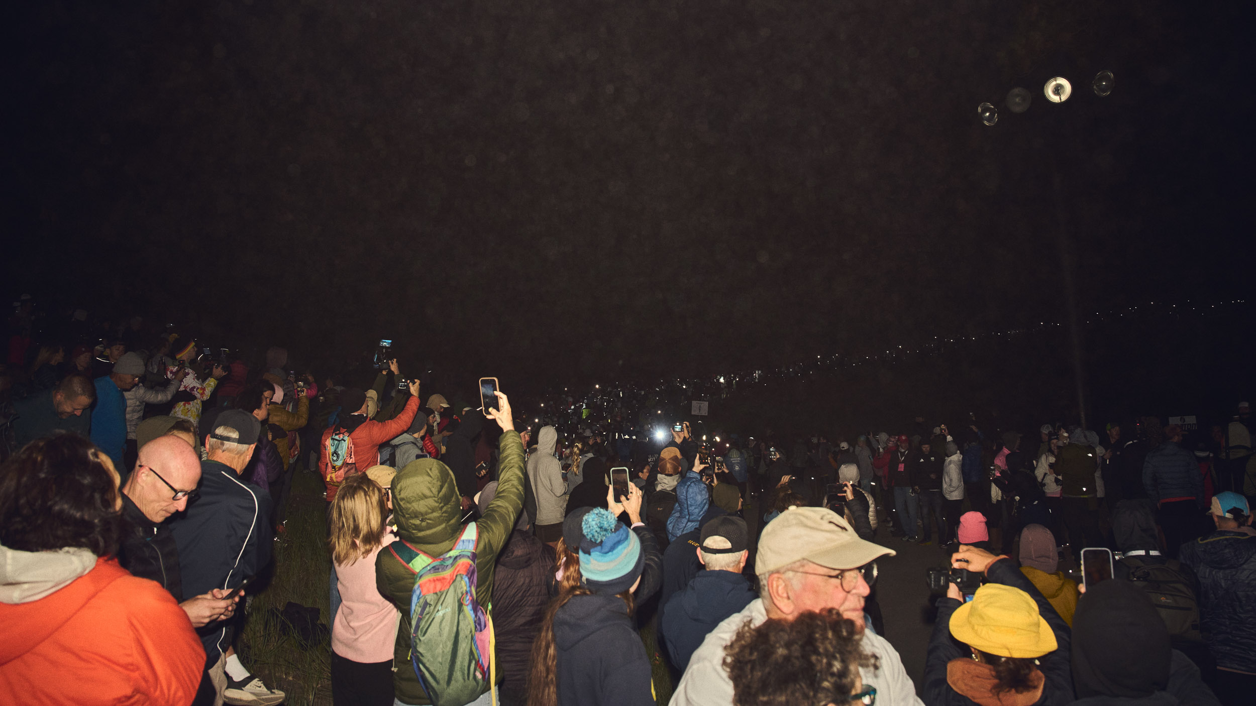 Spectators hold phones aloft as the Western States field climbs into the darkness.