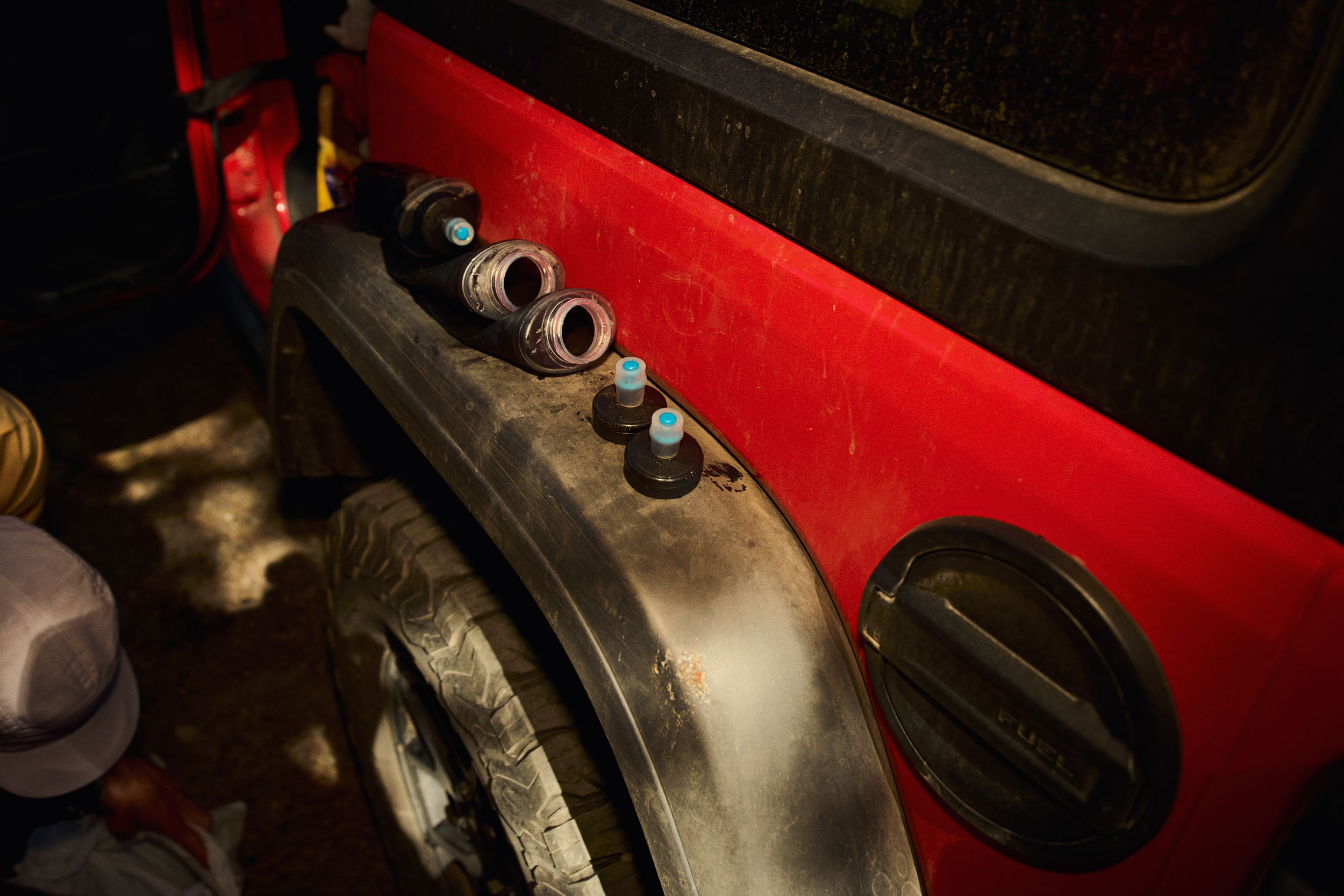 Soft hydration flasks are lined up on the dusty wheel arch of a support vehicle.