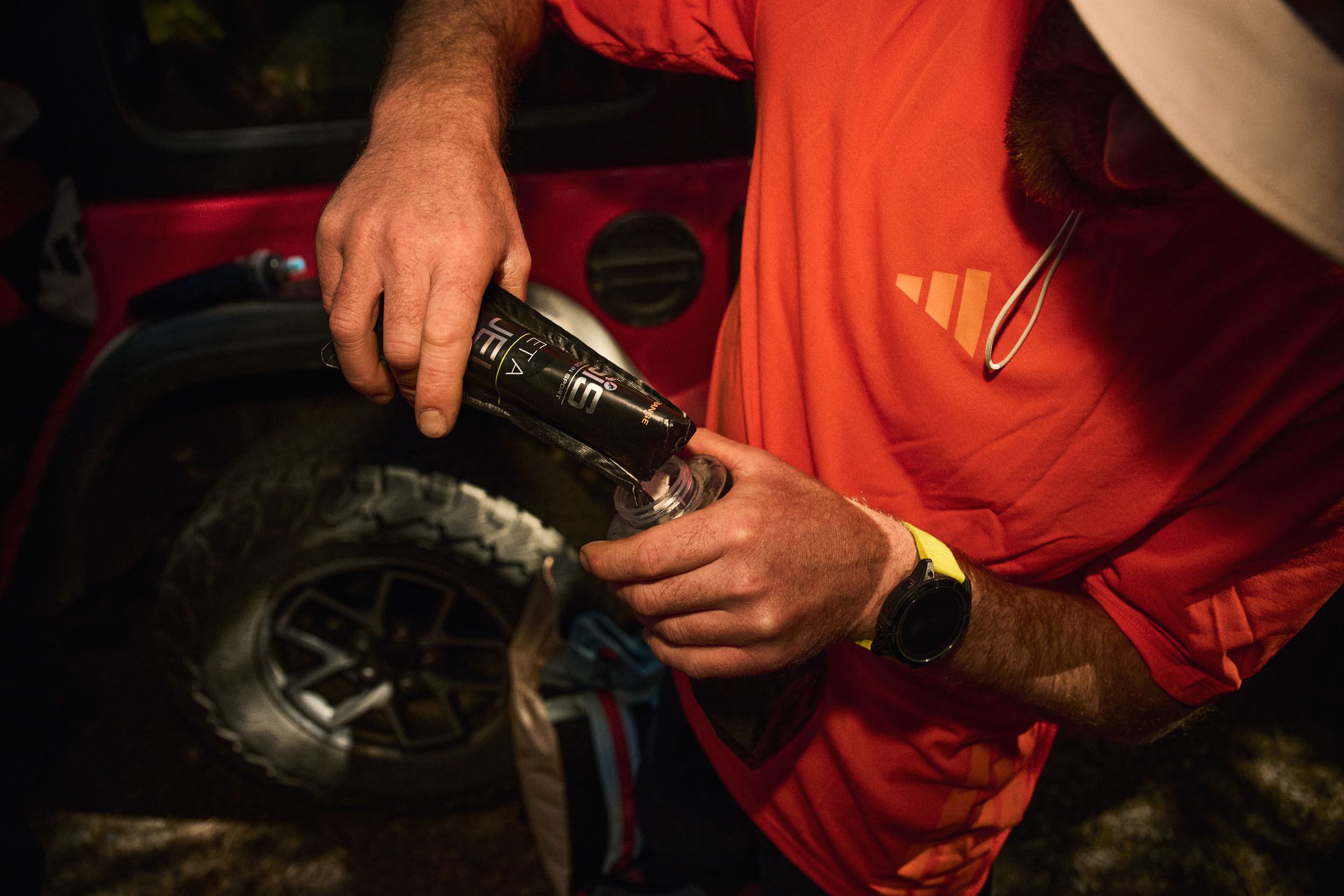 Crew member decants race nutrition into a soft flask beside the support vehicle.