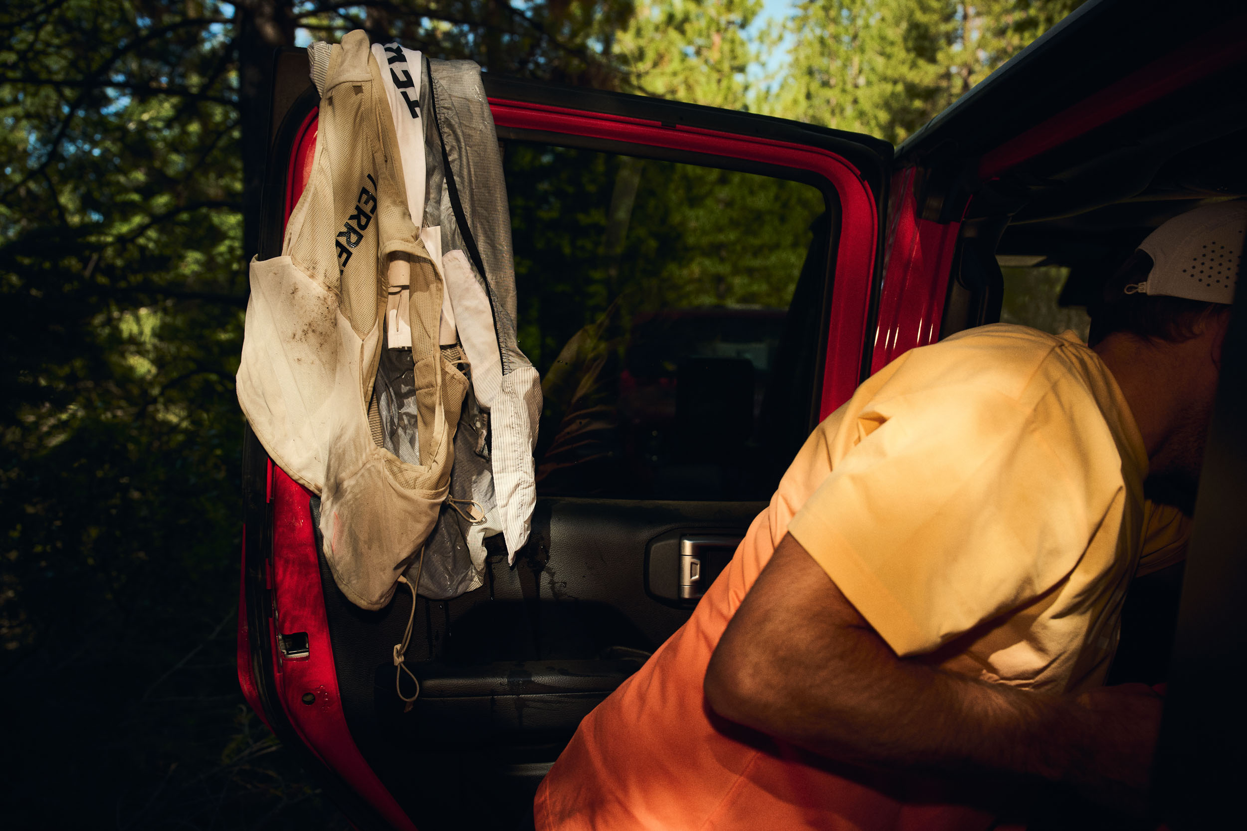 Mud-stained Adidas TERREX hydration vests hang from the door of a red Jeep.