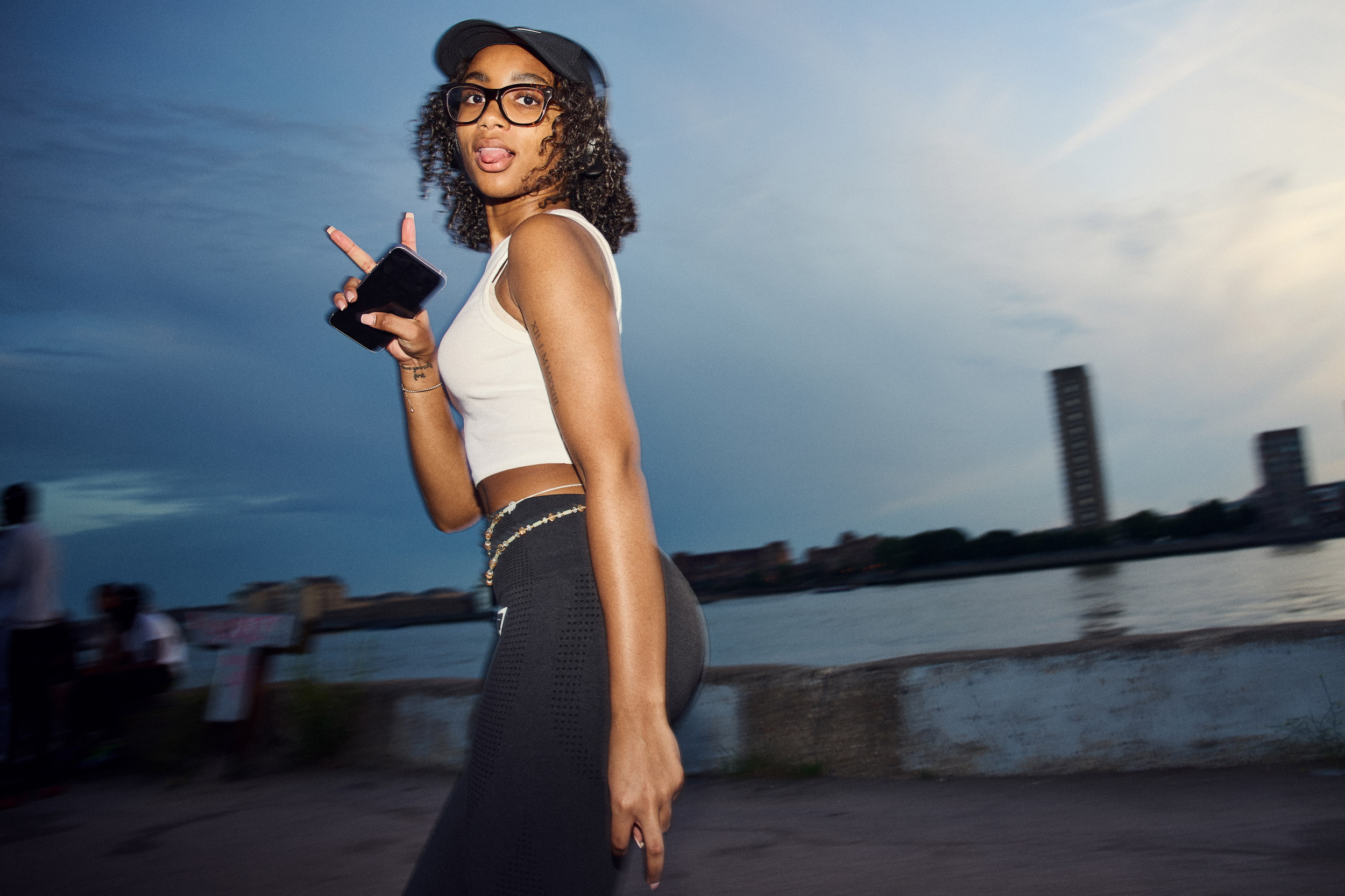 A skater turns to the camera with a peace sign, the Thames behind her at dusk.