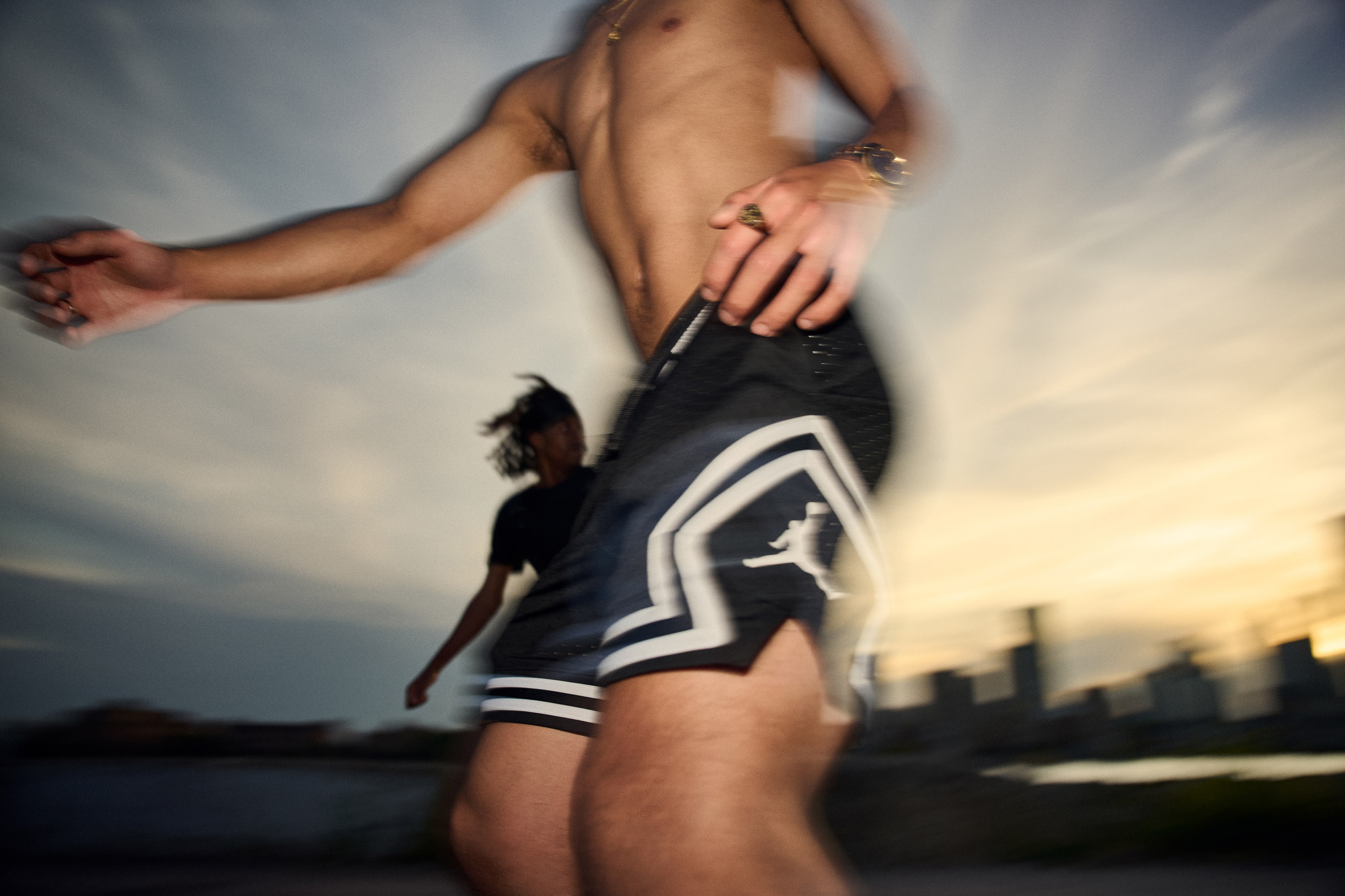 A skater passes close to the camera in a blur, the river and dusk sky behind.
