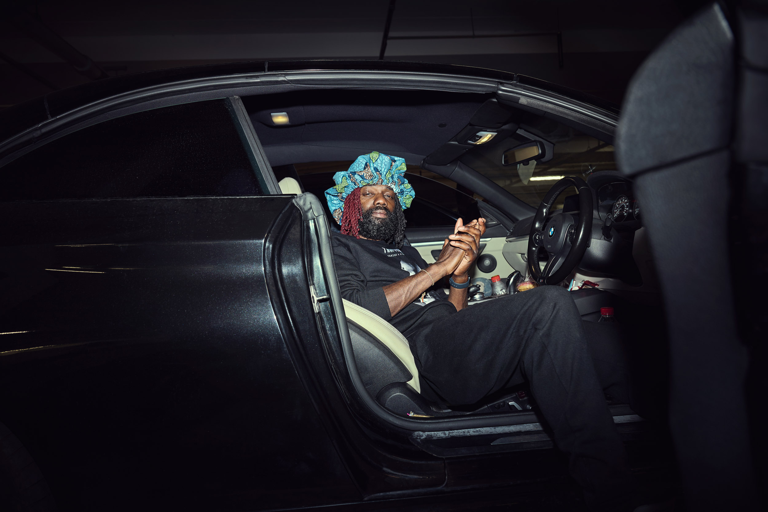 A skater sits in the driver's seat with the door open, watching the session from his car.