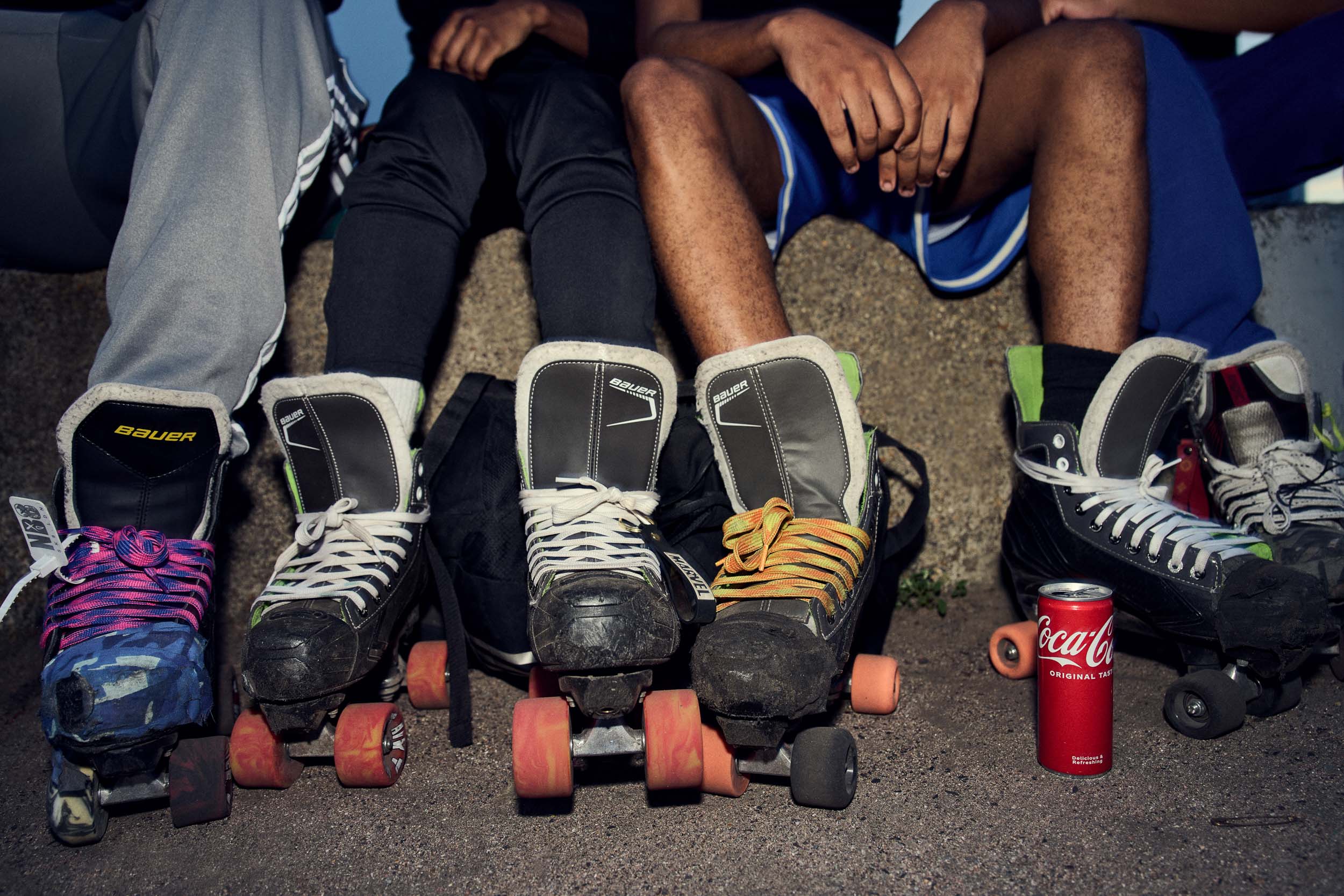 Four pairs of quad skates line up under the wall where their owners sit.