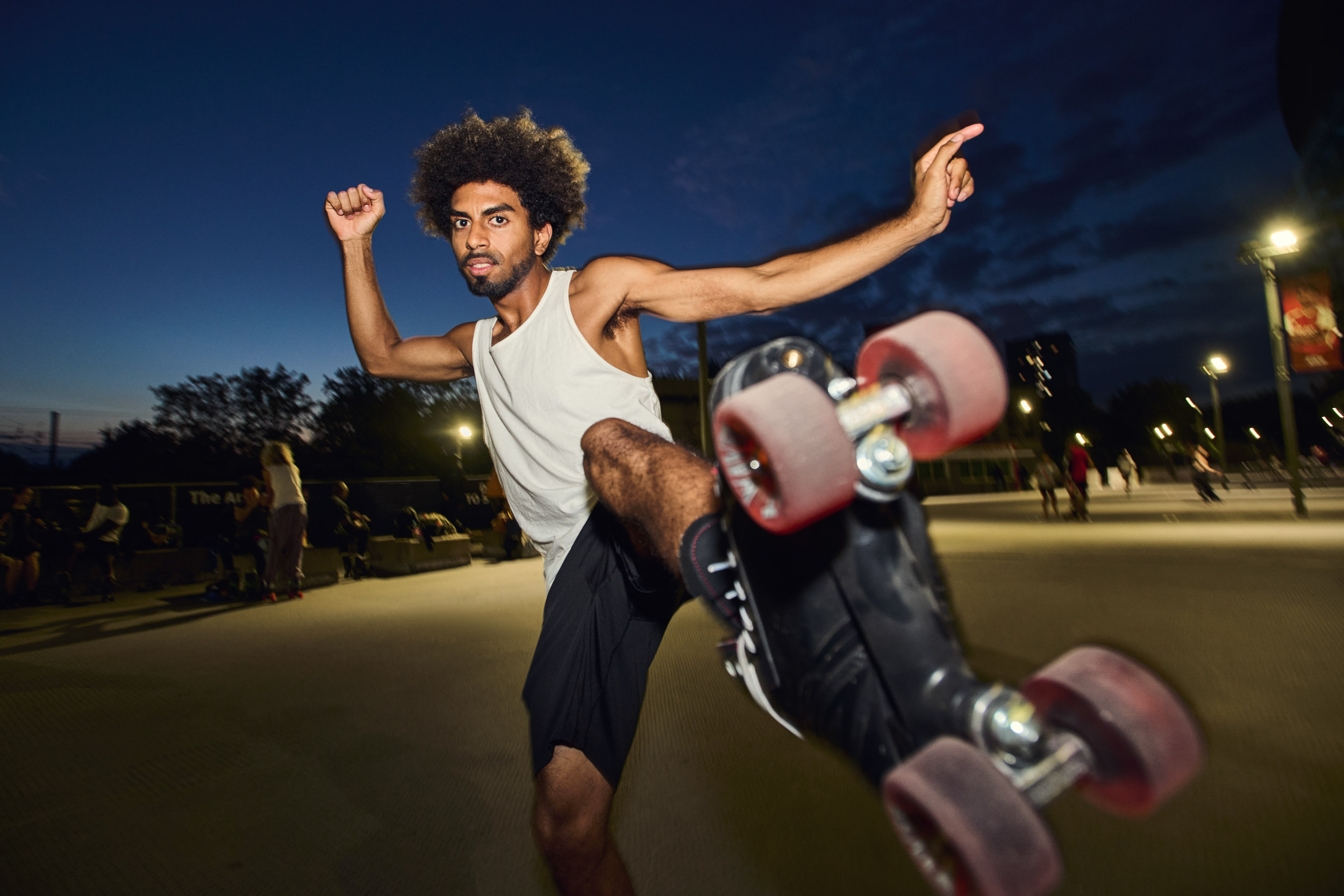 A skater swings a leg high, his wheels almost touching the lens against the dusk sky.