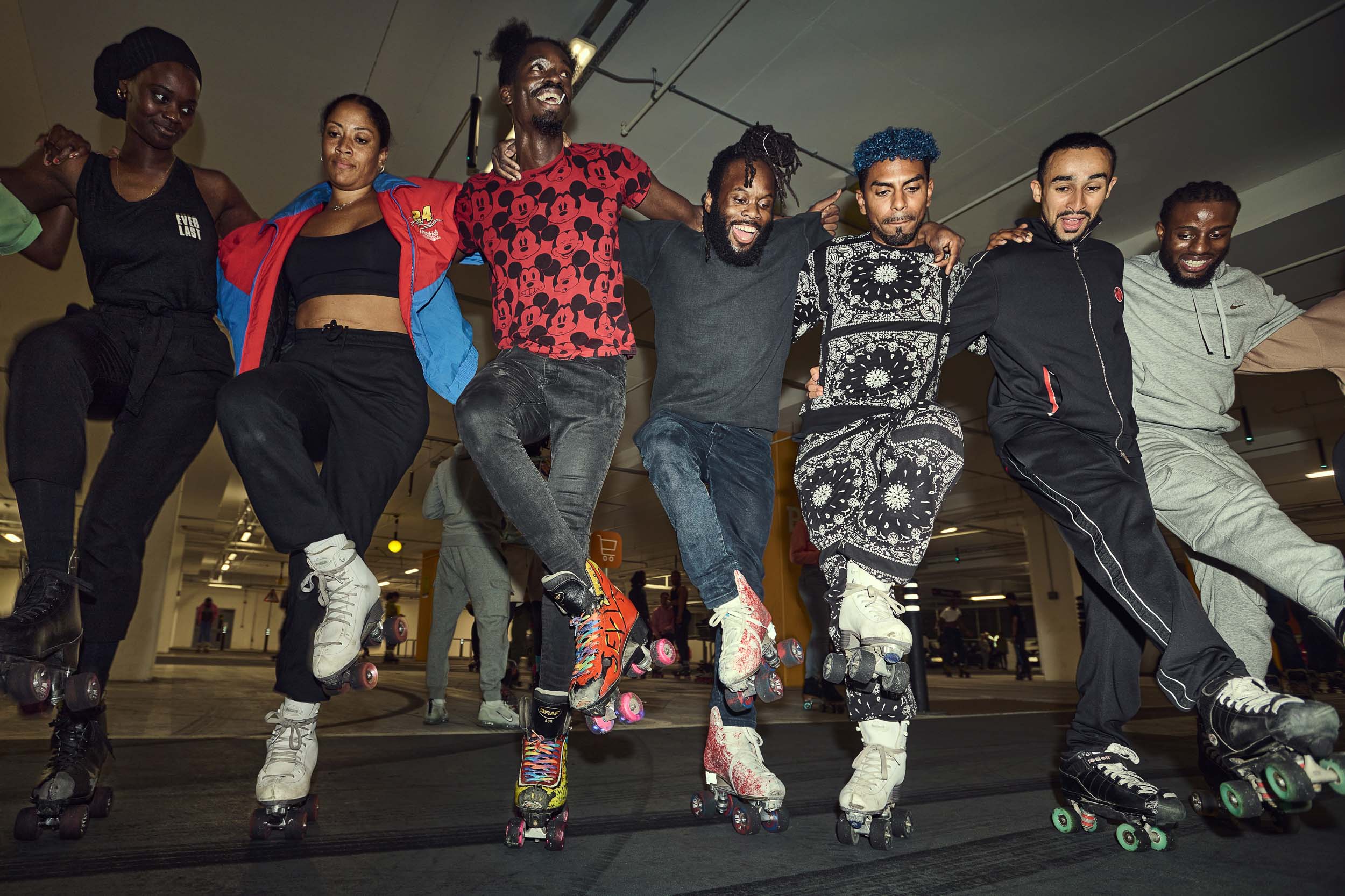 Seven skaters from the LDN on 8 community line up arm in arm with their legs raised in the car park.