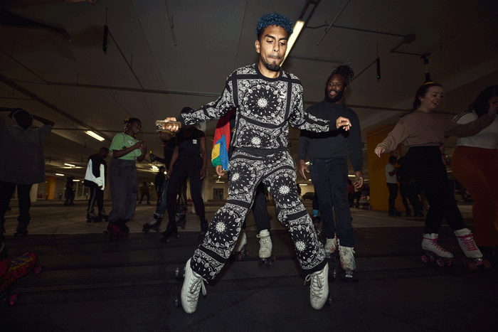 Roller skaters dropping into floor moves and handstands as the crowd watches in a Vauxhall car park.