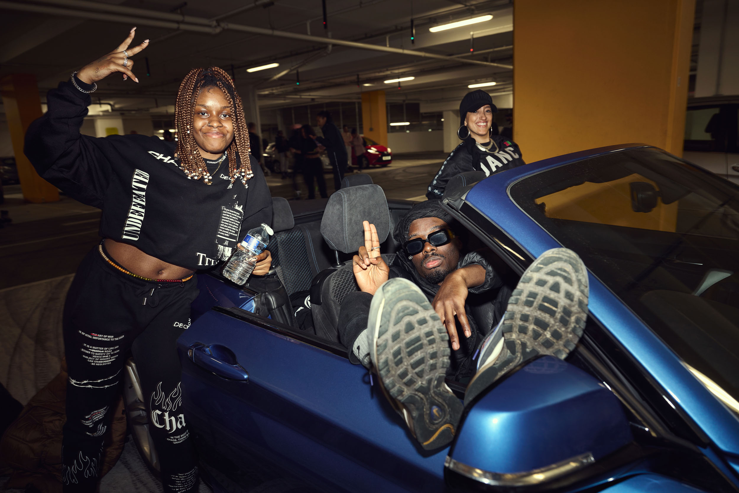 Three friends gather around a blue convertible parked in the middle of the session.