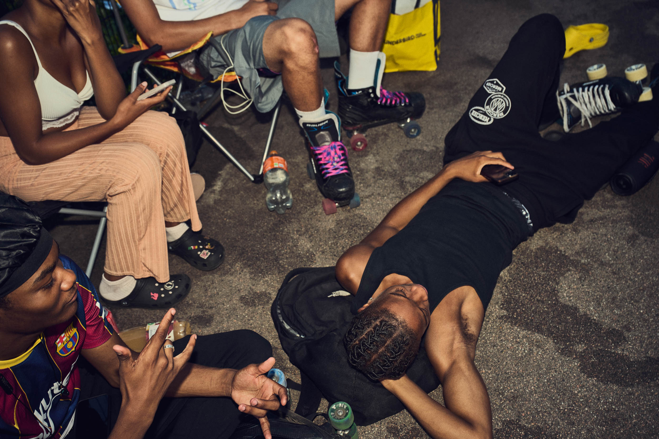Friends sit out a session together with skates, drinks and bags around them.