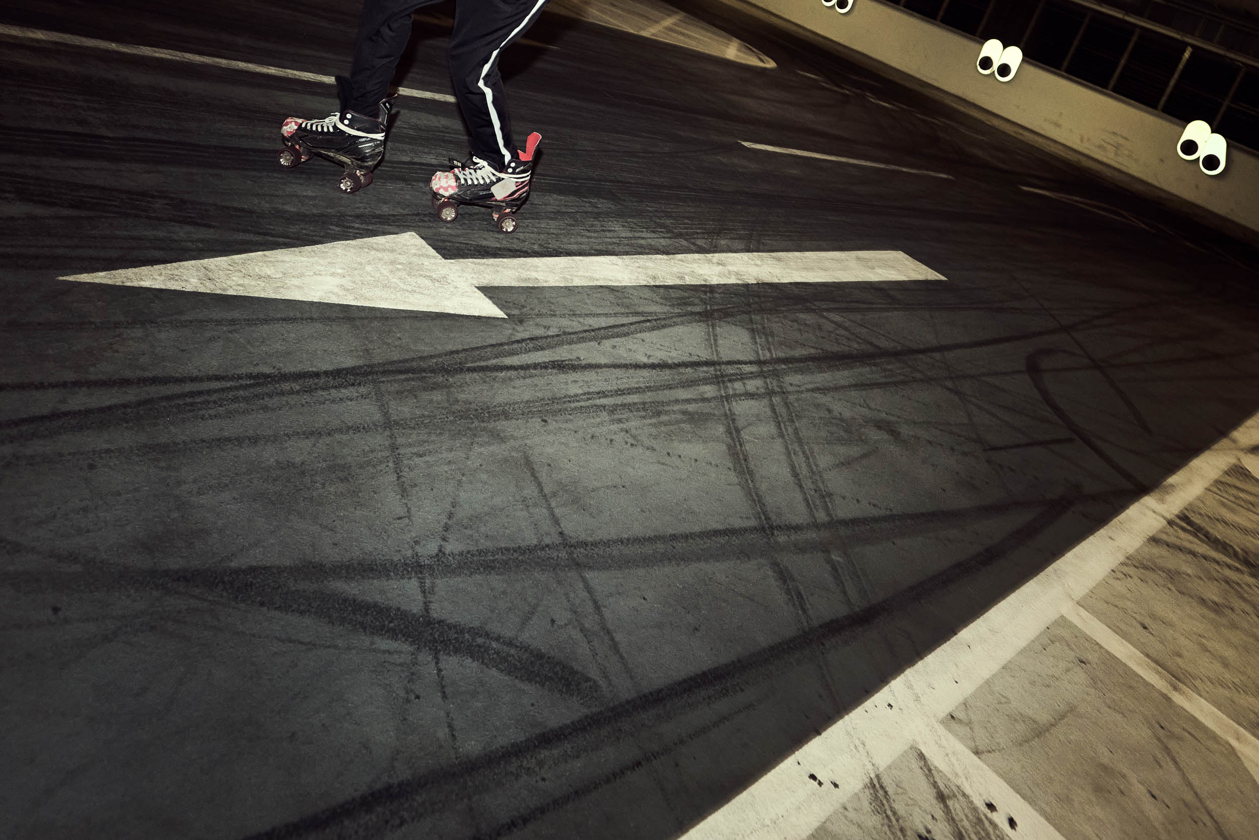 Quad skates roll across a painted floor arrow and tyre marks in the car park.
