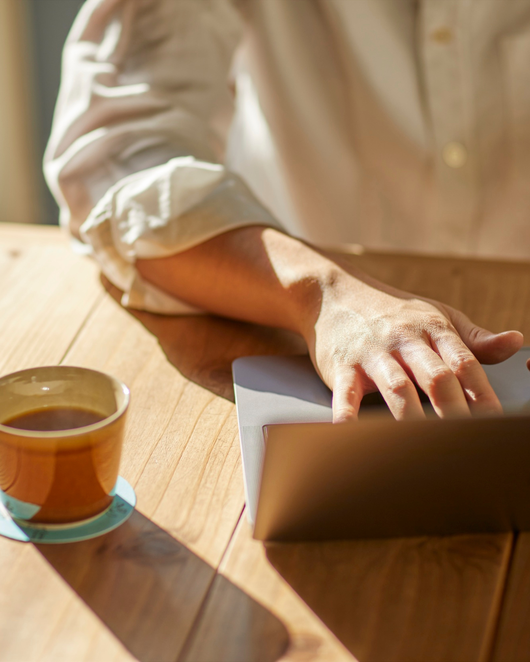 Konzentriert tippende Hand auf einem Laptop mit einer Tasse Kaffee daneben