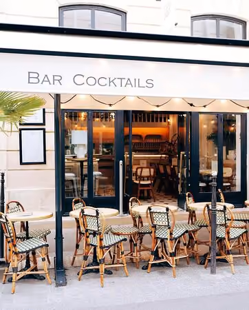Facade of a cocktail bar with outdoor terrace and several woven wicker tables and chairs.