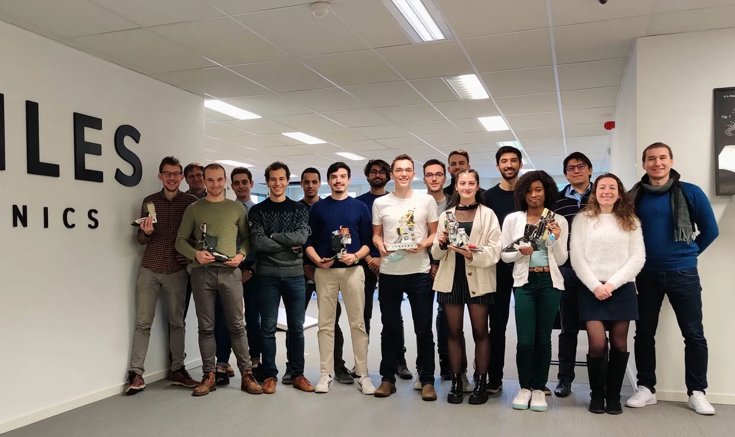 Team of Axiles Bionics standing in the Brussels office holding various prototype of prosthetic devices, smiling at the camera.