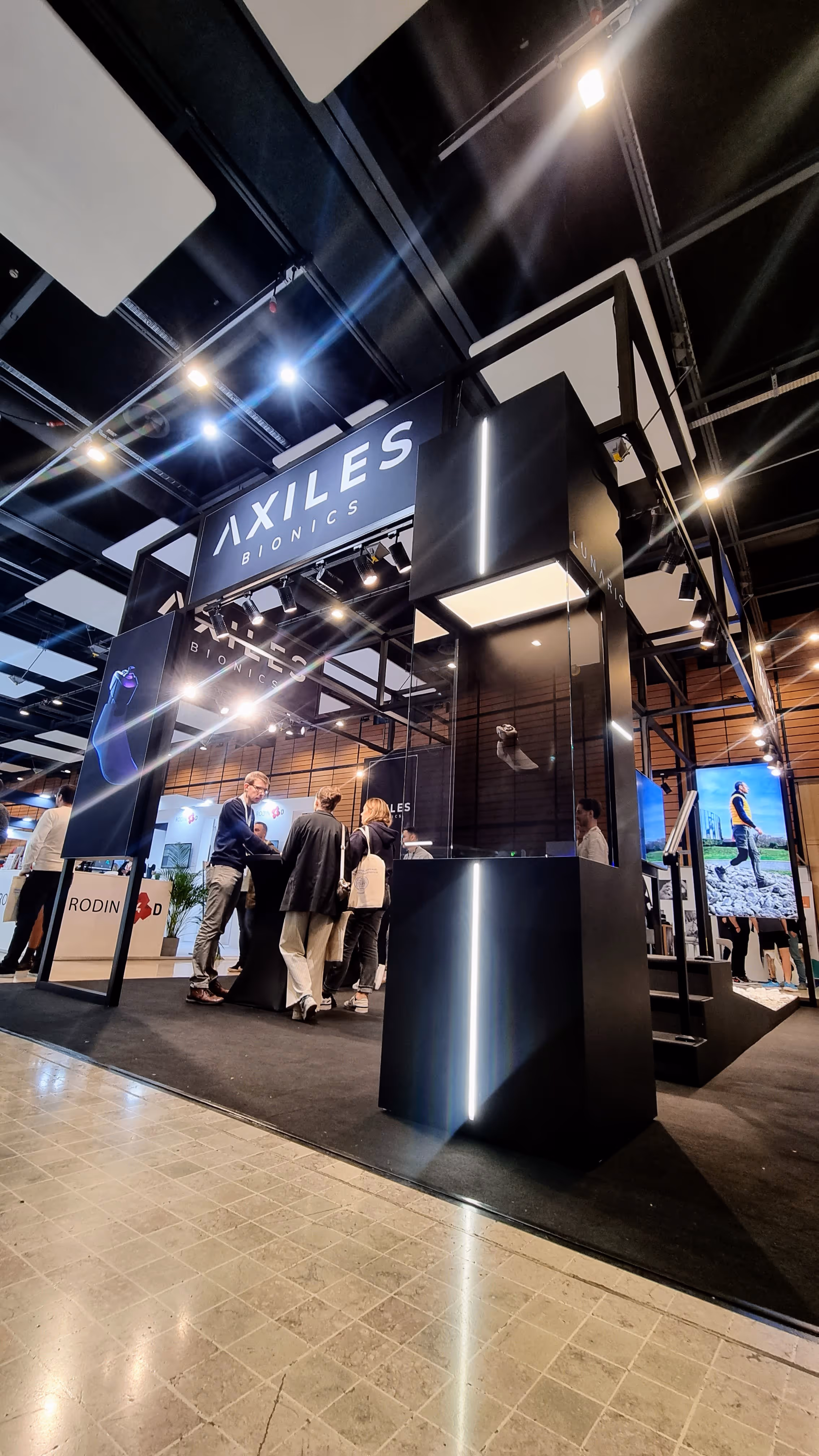 Trade show booth for Axiles Bionics with people discussing near a display case labeled Lunaris.
