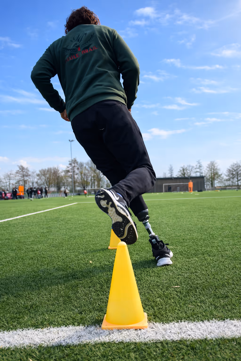 Person with a prosthetic leg navigating yellow cones on a green outdoor sports field.