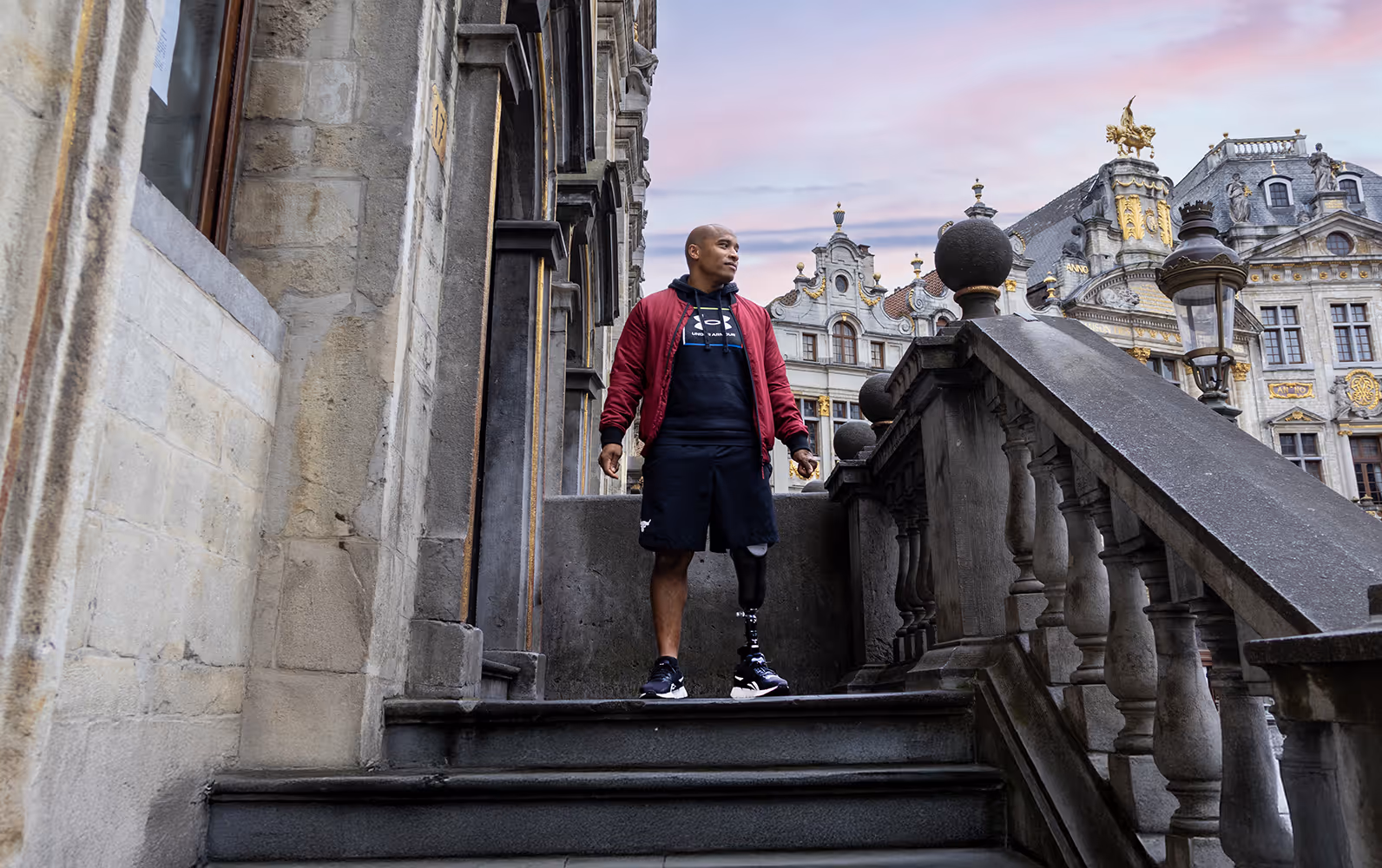 Man with a prosthetic leg standing on stone steps near historic ornate buildings at sunset.