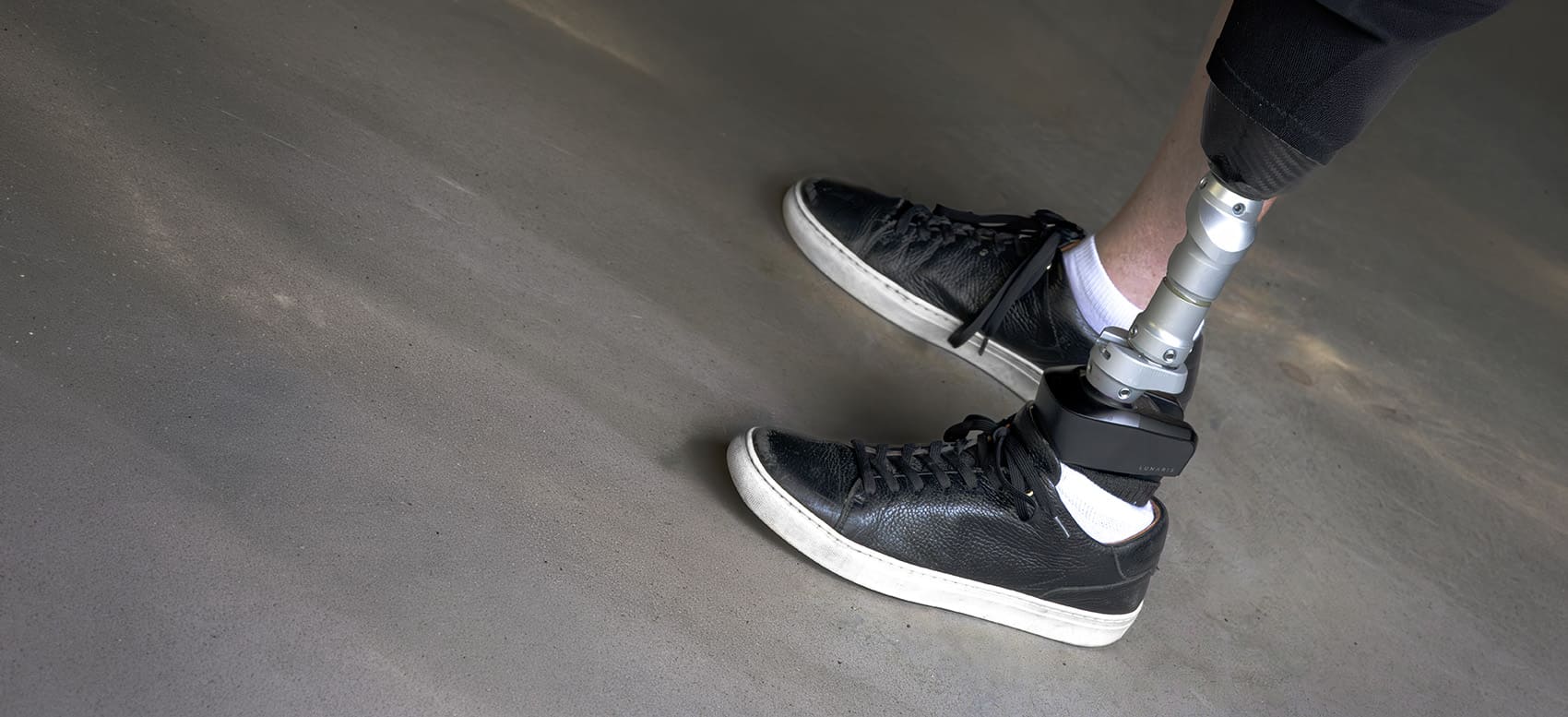 Person walking in a parking with a Lunaris prosthetic foot visible above a black shoe.