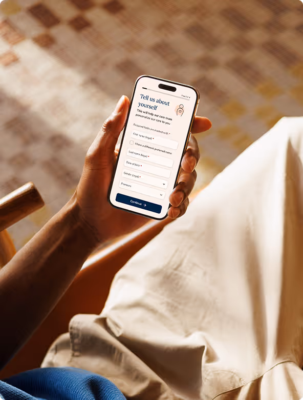 Hand holding a smartphone displaying a form to enter personal details including first and last name, gender, and pronouns.