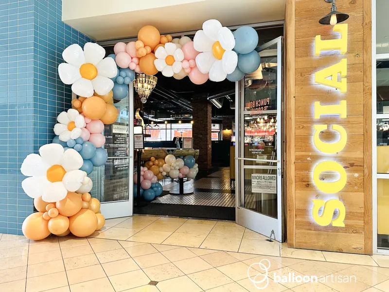 A spring themed balloon garland arch with flowers on it.