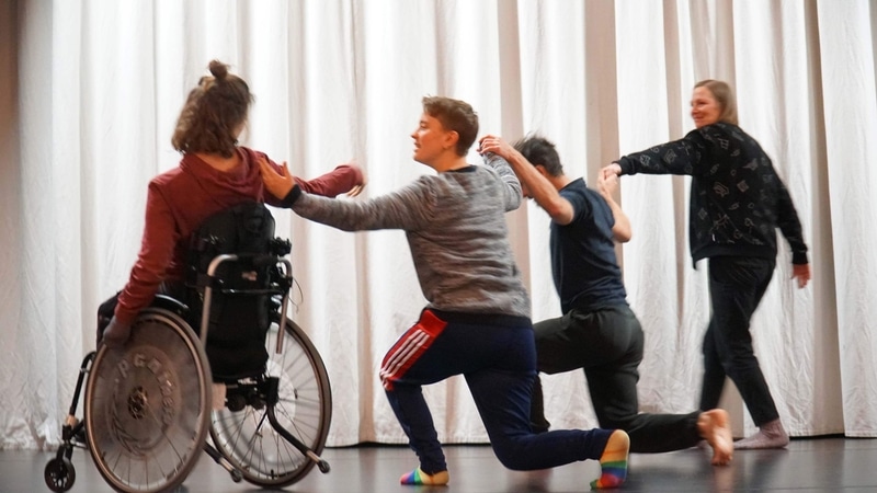 Fyra personer syns med ryggen mot kameran, dansande tillsammans. De har format en linje och lagt händerna på varandras axlar. Till vänster sitter en tjej i en rullstol - det är Karin Delen, dansare i ShareMusics dansensemble. Till höger om henne ser vi en tjej i ett utfallssteg med ena foten framför sig och den andra bakom. Det är Liv dahlstrand, musiker i Elefantöra. Till höger om henne syns en man i samma ställning, det är koreografen Wagner Moreira. Han håller hand med en kvinna som står till höger om honom och ler. Hon heter Anna Gustavssson och är tonsättare.