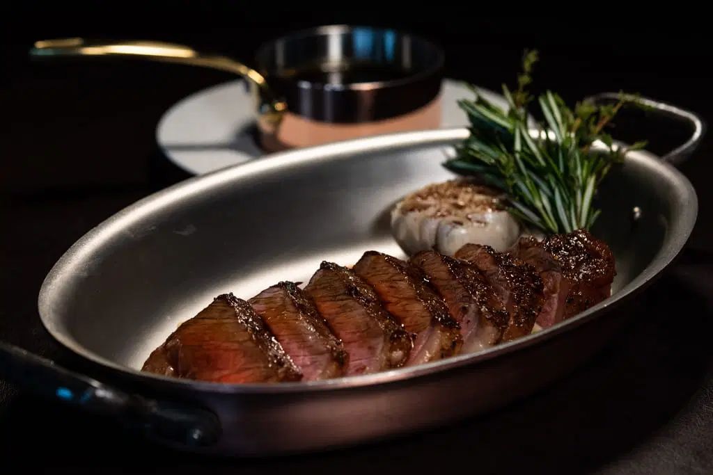 Plated sliced steak served in a copper pan with rosemary