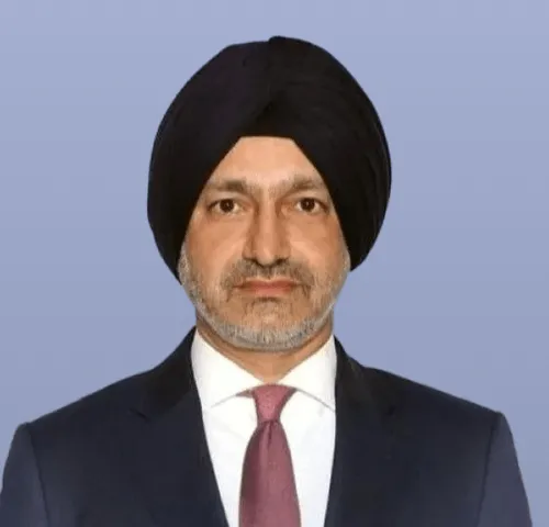 Man wearing a black turban and a dark suit with a white shirt and pink tie on a blue background.