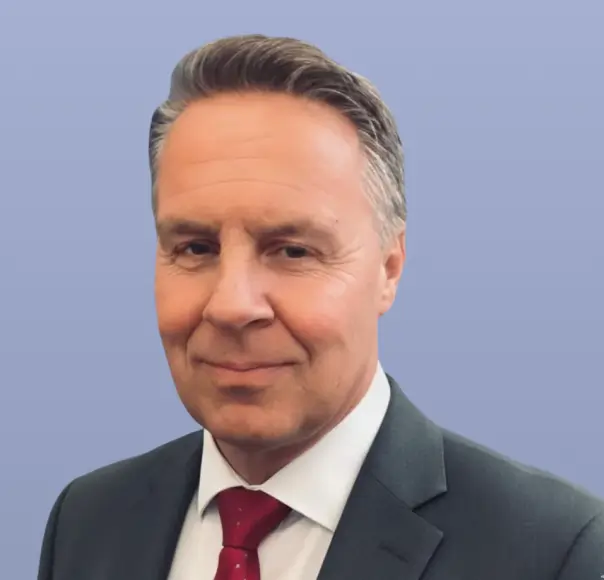 Middle-aged man in a suit and red tie with short grayish hair and a slight smile on a blue background.