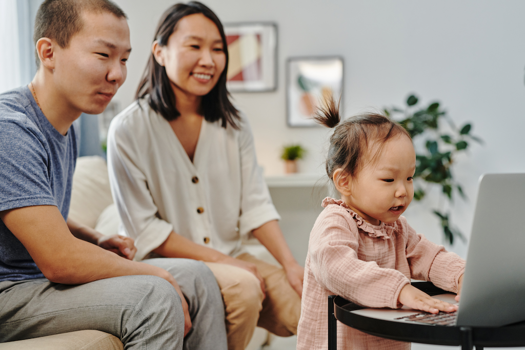 A racialized couple smiling as their toddler plays on a laptop