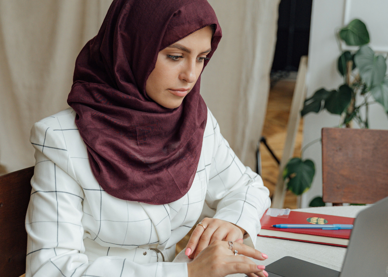 A woman wearing a hijab is scrolling on a laptop.