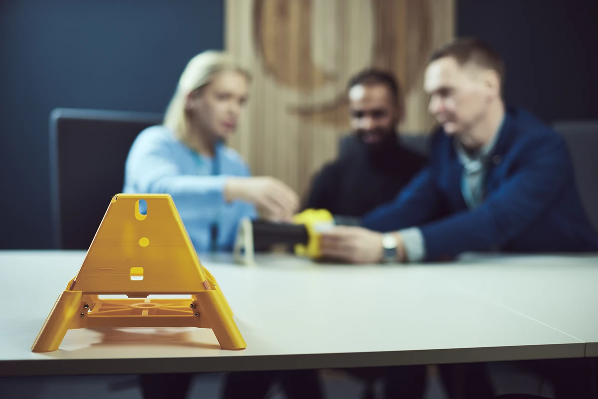 Yellow triangular support structure on a table with three people in the background working together.