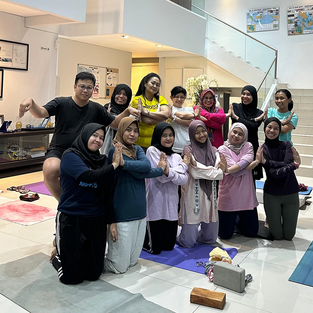 Group of diverse people gathered on yoga mats indoors, posing with hands in prayer or crossed in front of their chests.