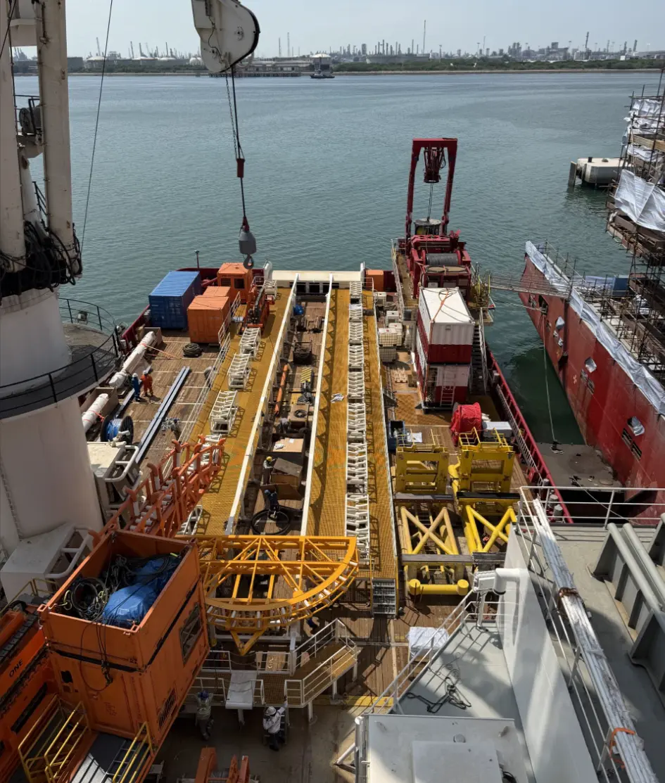 View of an industrial ship deck with heavy equipment and cranes by calm harbor waters.