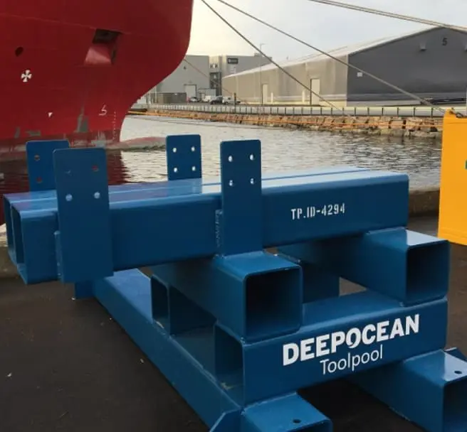 Blue steel container labeled DEEPOCEAN Toolpool on dock next to red ship and water.