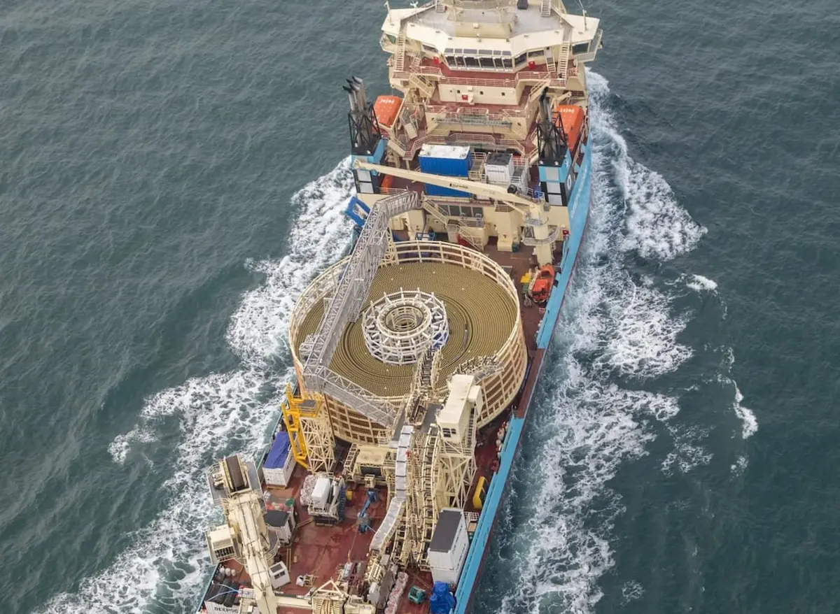 A large blue and cream offshore ship with a helipad and cable spool on the deck, moving through water.