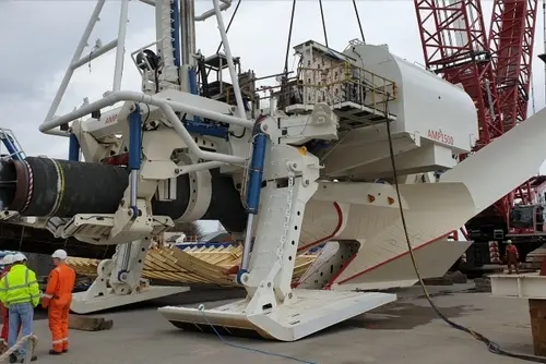 Industrial machinery with large white blades, two workers in safety gear standing nearby.