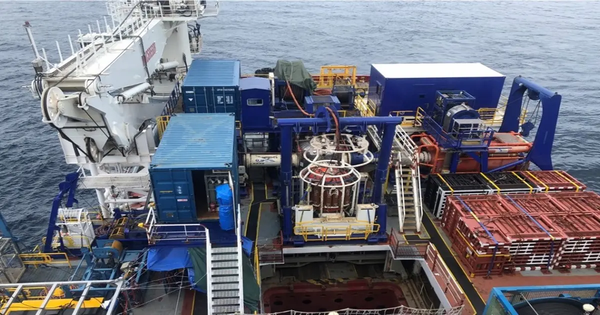 Top view of a ship deck with blue and red industrial equipment and containers on open sea.
