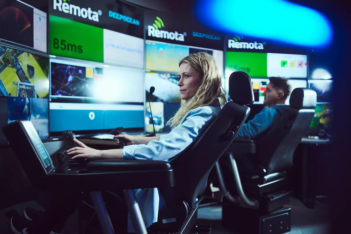 Two operators using joysticks in a control room with large video monitors displaying Remota DeepOcean data.