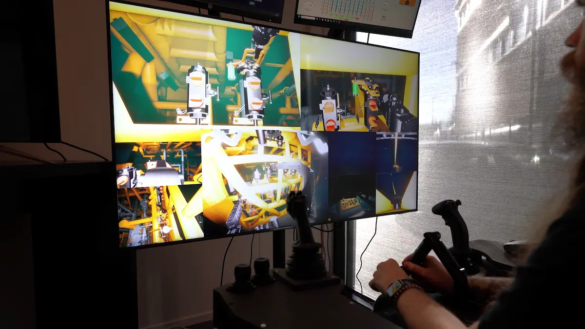 Person operating a multi-role simulator with multiple screens showing industrial equipment controls.