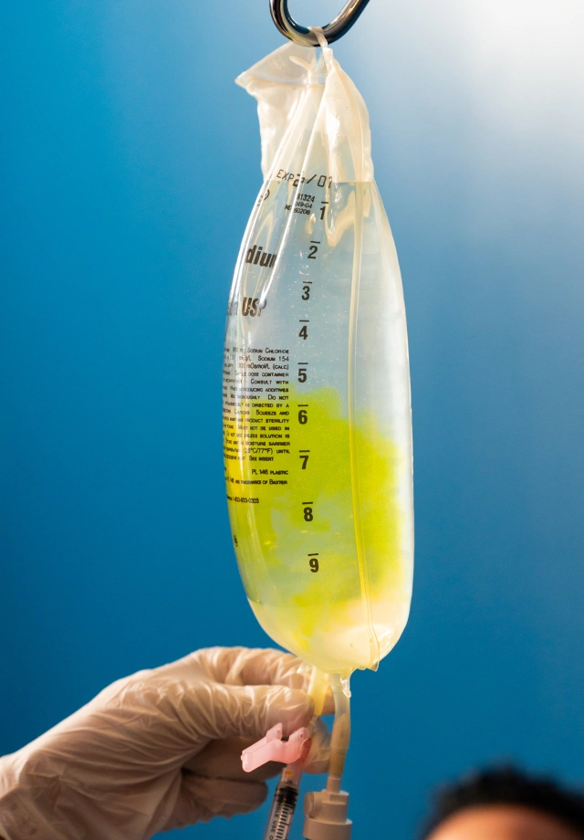 Gloved hands reaching up to adjust the flow of an IV drip bag