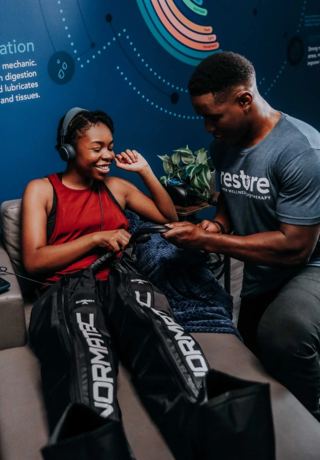 Smiling woman enjoying compression therapy boots while Restore employee adjusts pressure settings