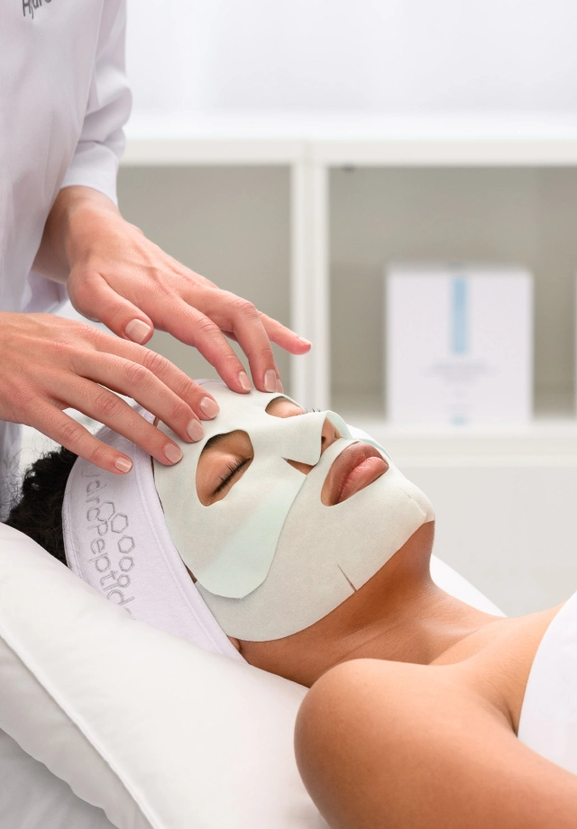 A woman receiving a custom HydroPeptide facial at Restore