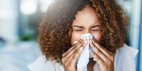 Image of a woman sneezing from ragweed allergies in front of ragweed.