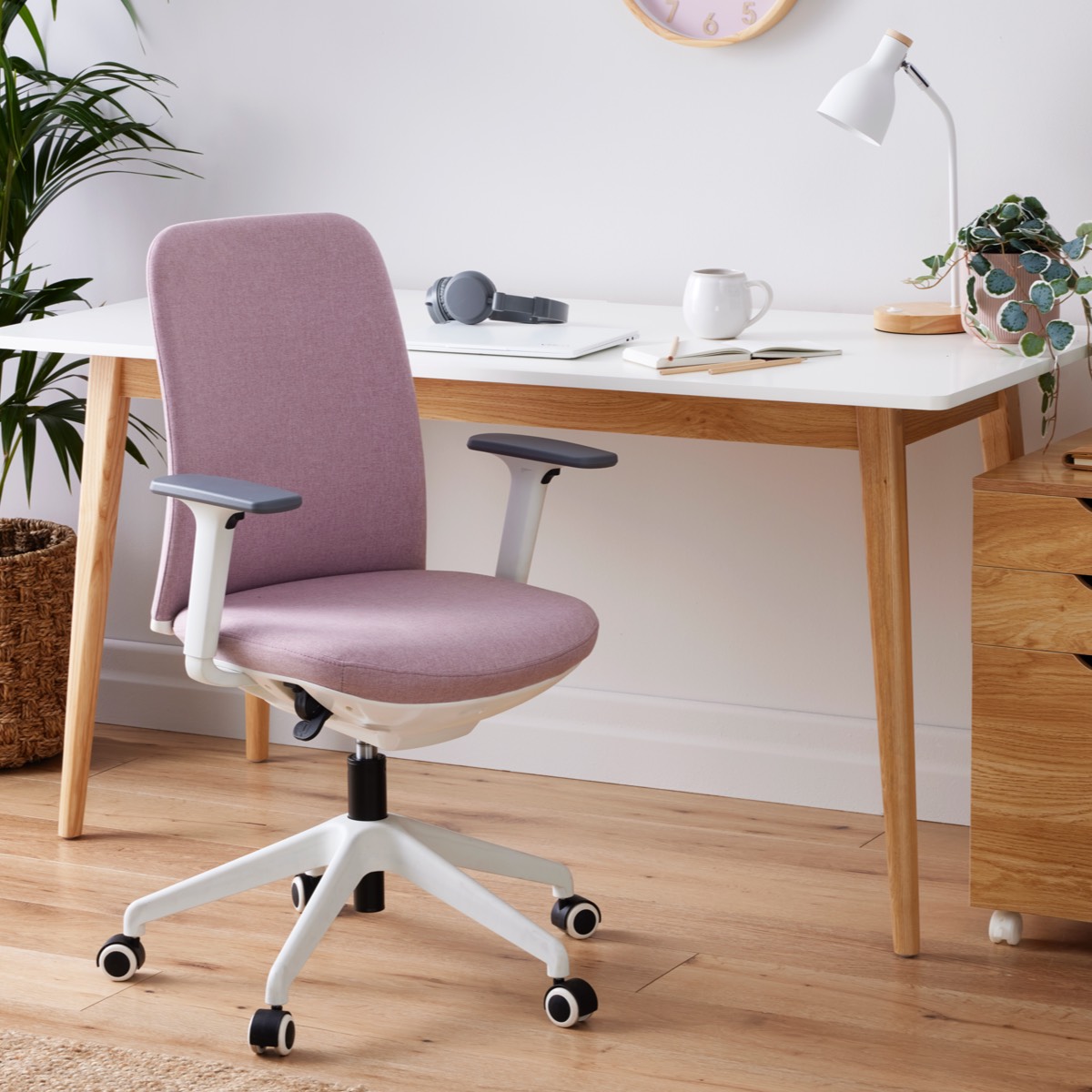 Pink ergonomic office chair with white frame and adjustable armrests, in a modern home office setup.