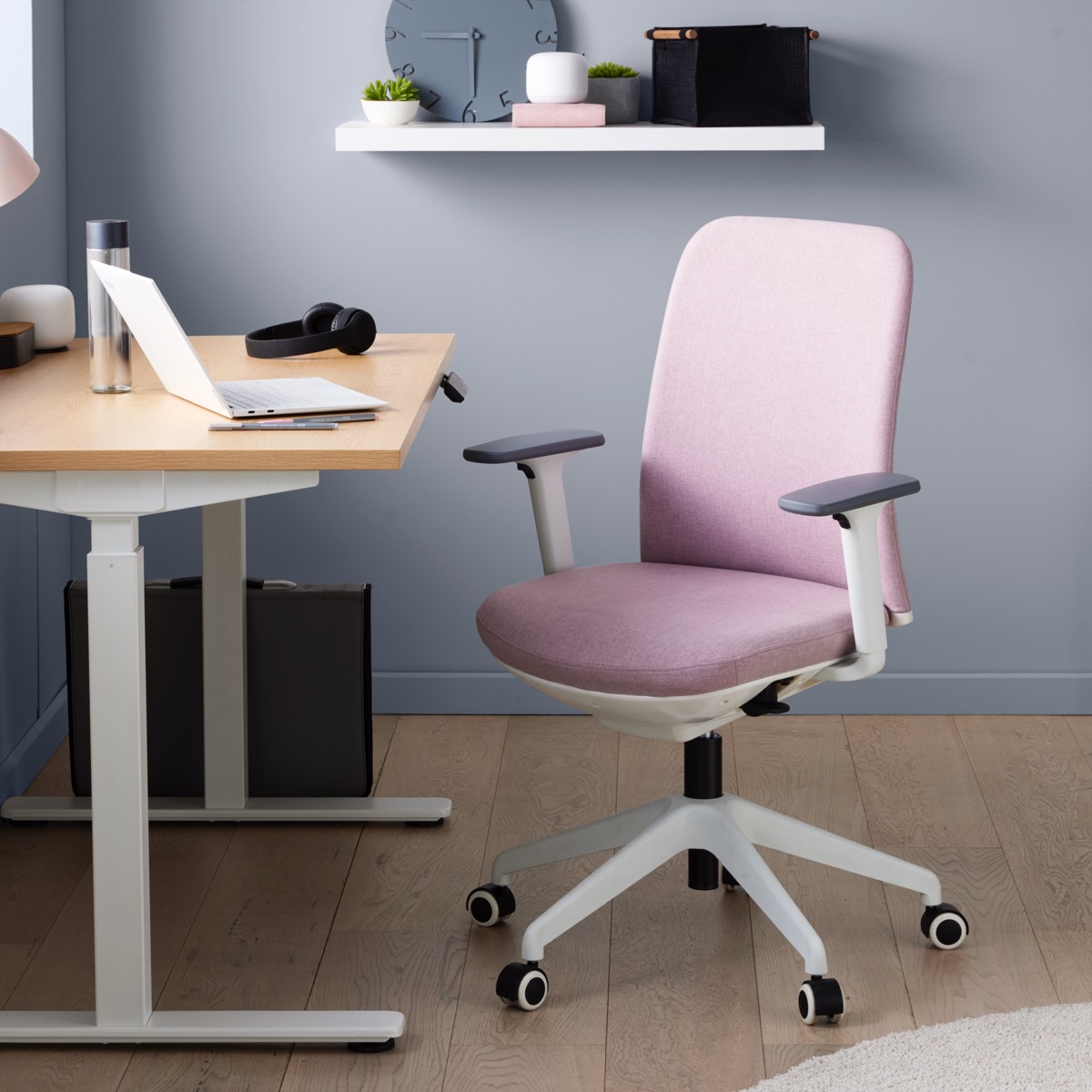 Pink ergonomic office chair with white frame and adjustable armrests, in a modern home office setup.