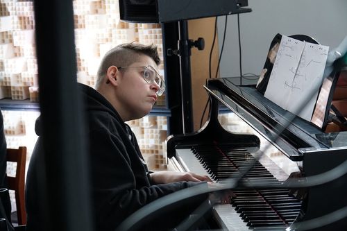 Ewe spelar på en miniflygel, syns i profil. Hon har svarta kläder på sig och glasögon med tunna metallbågar. Hon har en fokuserad blick och tittar åt sidan, liksom ovanför kameran. Högtalare och sladdar syns i periferin.