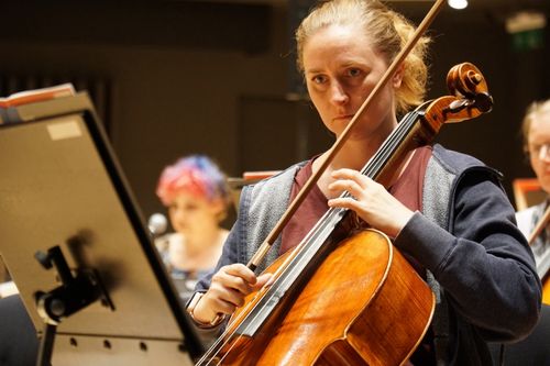 En kvinna spelar cello med mycket fokuserad blick på noterna framför henne.