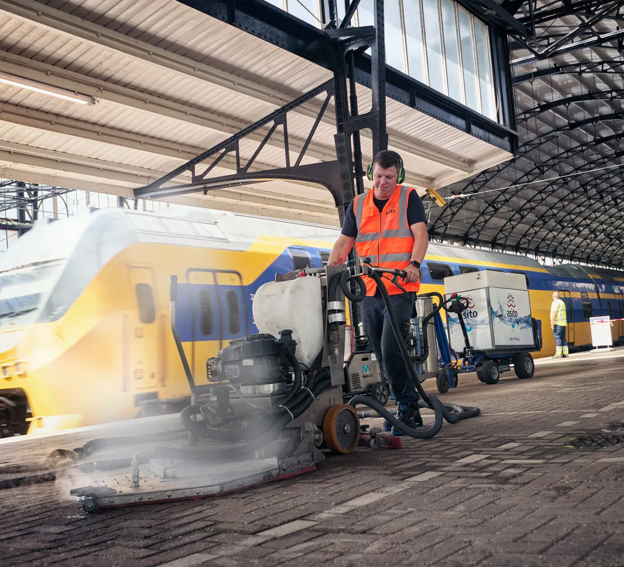 Schoonmaker van Asito reinigt met een schrobmachine het perron van een treinstation