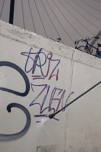 Close-up van een Asito-medewerker die met een hogedrukreiniger graffiti verwijdert van een betonnen muur